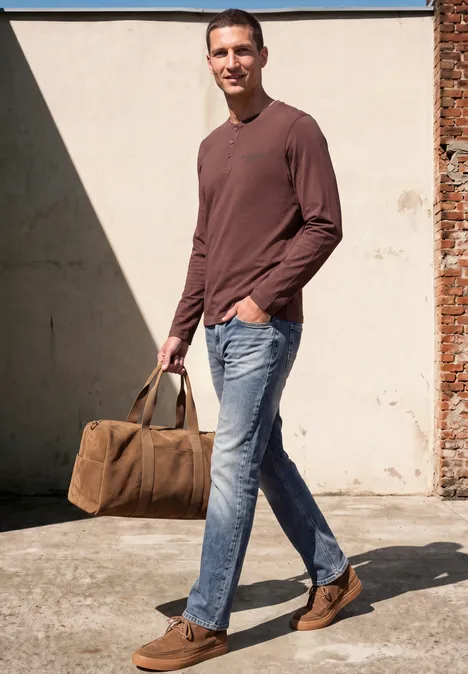 Een man in een bruin shirt, jeans en bruine schoenen draagt een canvas tas en loopt glimlachend.