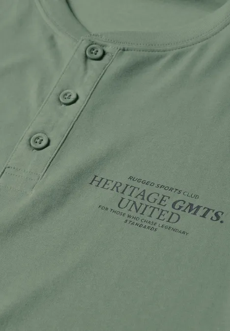T-shirt vert avec patte de boutonnage et inscription 'HERITAGE GMTS. UNITED'