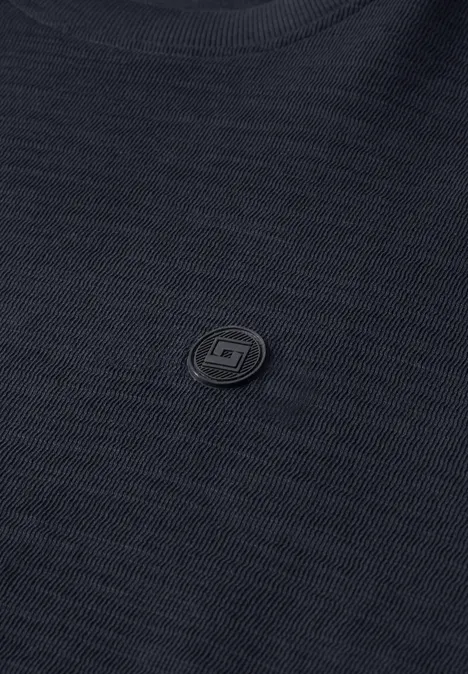 Nahaufnahme eines schwarzen Stoffes mit feiner Textur und kleinem, rundem Logo in der Mitte.