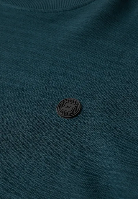 Ein dunkelgrüner Pullover mit feiner Struktur und einem kleinen schwarzen, runden Logo-Emblem auf der Brust.