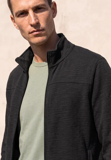 Langarm Jacke mit Stehkragen basic black Ein Mann mit kurz geschnittenem Haar trägt eine schwarze, leichte Steppjacke über einem grünen T-Shirt.