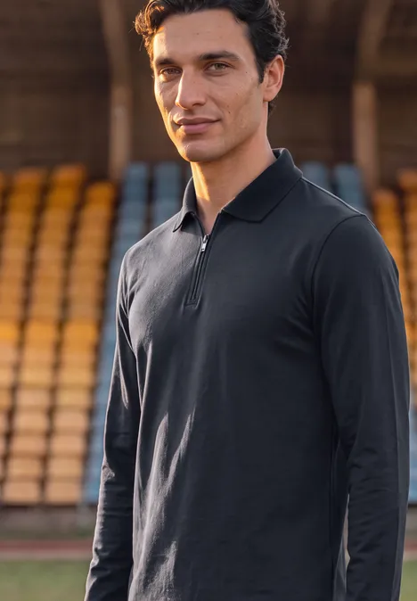 Ein sportlich gekleideter Mann in schwarzem Langarm-Polo steht vor Stadiontribünen.