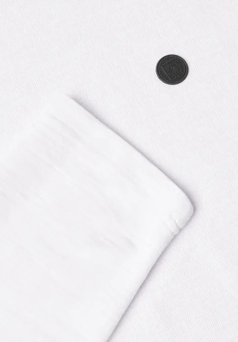 Gros plan d’un textile blanc avec ourlet visible et un petit bouton noir sur fond blanc.