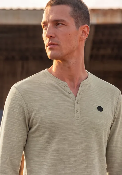Mann in hellem Henley-Shirt blickt in die Ferne vor rustikalem Hintergrund