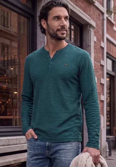 Ein Mann in grünem Langarmshirt und Jeans steht lässig auf einer Stadtstraße.