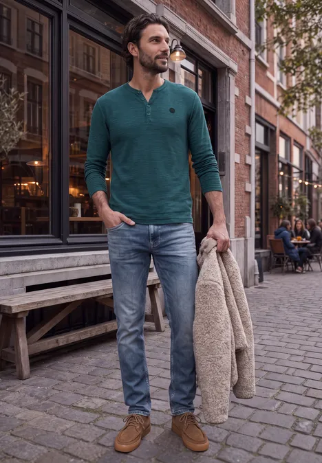 Ein junger Mann in grünem Pullover und Jeans schlendert entspannt mit Jacke durch eine Altstadtgasse.