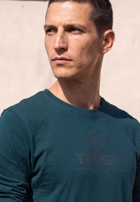T-shirt à manches longues avec imprimé ton sur ton dark fjord blue Homme aux cheveux courts portant un t-shirt vert foncé 'TOUGH' regardant vers la droite.