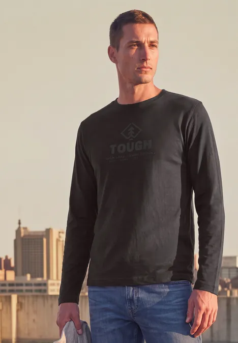 T-shirt à manches longues avec imprimé ton sur ton shadow brown Ein Mann trägt ein schwarzes Sweatshirt mit dem Aufdruck 'TOUGH' und steht auf einem Dach vor städtischer Kulisse.