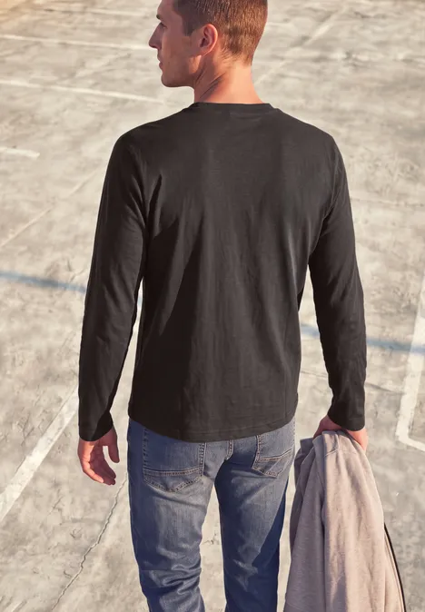 T-shirt à manches longues avec imprimé ton sur ton shadow brown Ein Mann in schwarzem Langarmshirt und Jeans steht auf einem Betonplatz und hält einen Mantel.
