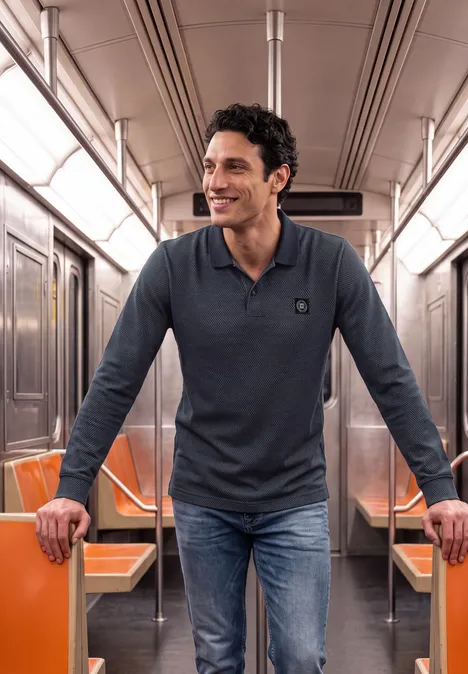 Ein lächelnder Mann in Jeans und Polo steht in einer U-Bahn mit orangefarbenen Sitzen.
