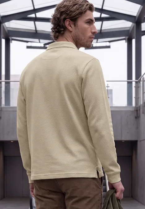 Ein Mann in beige Jacke von hinten in einem modernen Gang mit Glasdach, blickt über die Schulter.