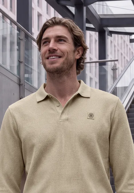 Ein lächelnder Mann im beigen Poloshirt steht vor einer modernen Glasfassade.