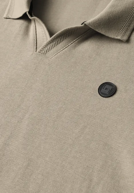 Nahaufnahme eines beigen Poloshirts mit Kragen und schwarzem Logo-Patch, betont die Struktur des Stoffs.