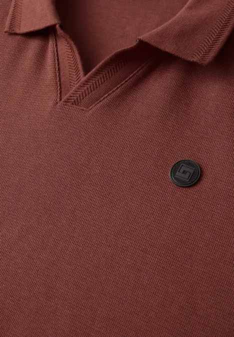 Braunes Poloshirt mit V-Kragen und kleinem runden Logo-Badge auf der Brust.