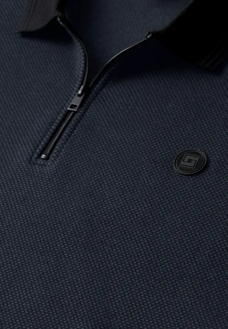 Detail eines dunkelblauen, strukturierten Polos mit halbem Reißverschluss und rundem Logo auf der Brust.