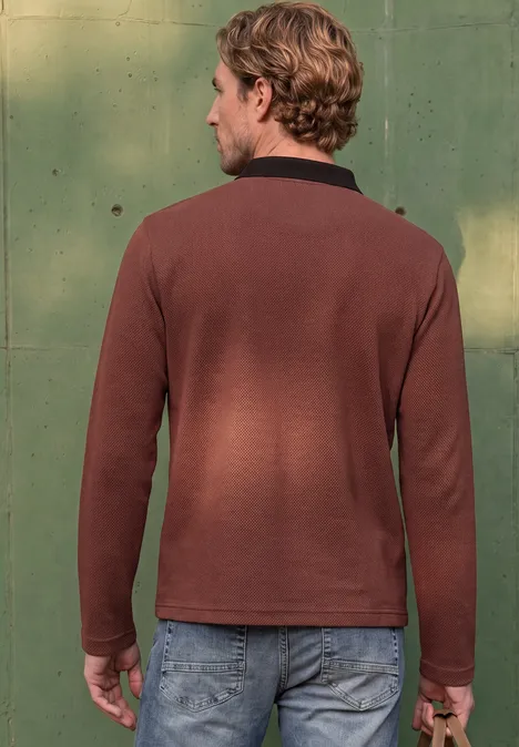 Mann von hinten in braunem Pullover und Jeans vor grünem Hintergrund.