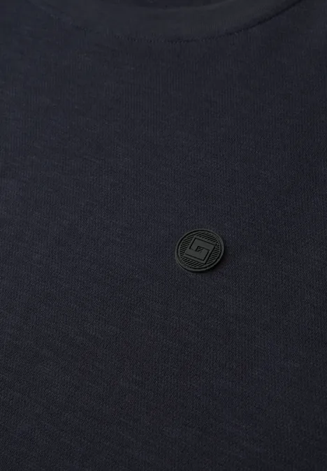 Gros plan sur un t-shirt sombre avec un petit logo circulaire discret au centre.