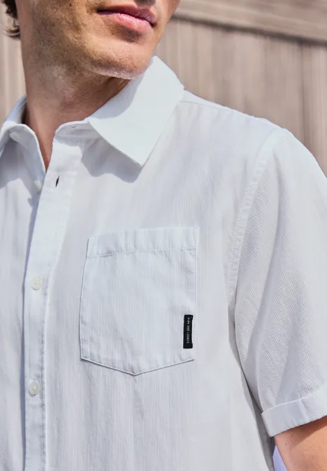 Mężczyzna nosi białą koszulę z krótkim rękawem, kieszenią na piersi i czarną metką.
