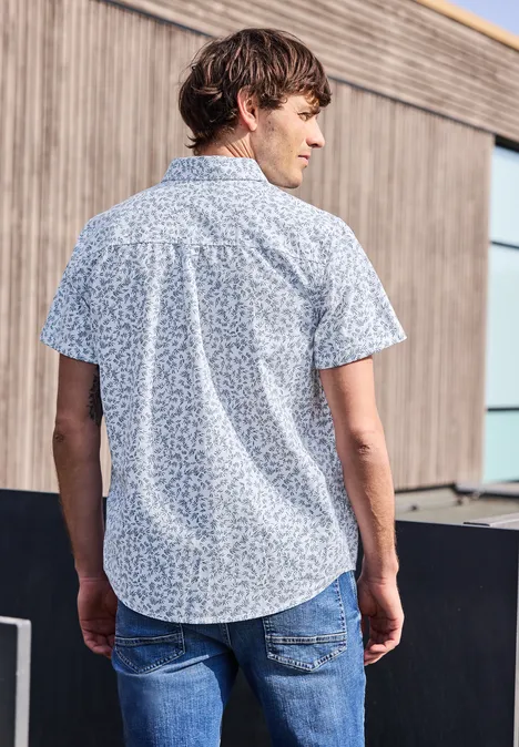 Mężczyzna tyłem do kamery ma na sobie niebieską, wzorzystą koszulę z krótkim rękawem i dżinsy.