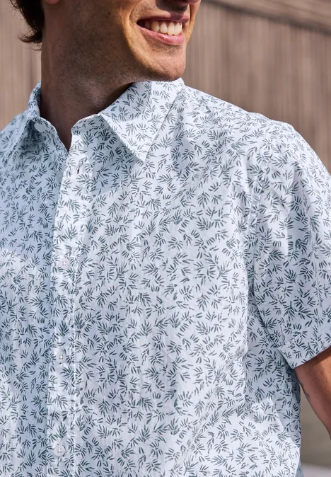 Mężczyzna uśmiechnięty w białej koszuli z niebiesko-zielonym wzorem liści.