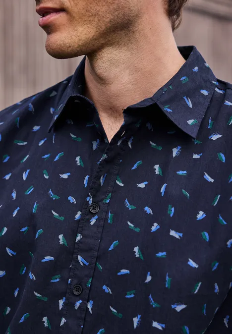 Mężczyzna ma na sobie granatową koszulę z drobnymi, niebiesko-zielonymi motywami ryb.