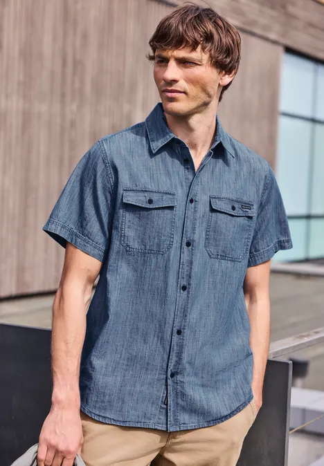 Mężczyzna w jeansowej koszuli z krótkim rękawem przed nowoczesnym budynkiem