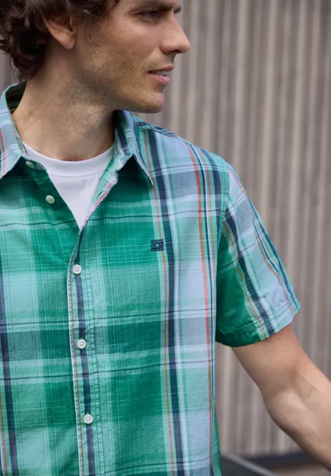 Iemand draagt een groen geruit hemd met korte mouwen over een wit T-shirt.