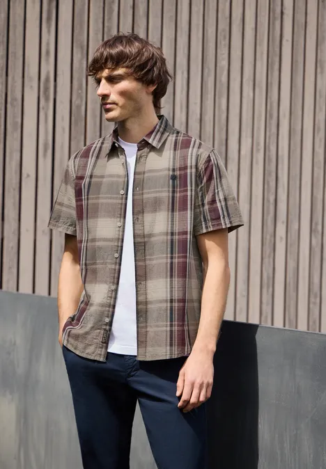 Man in geruit kort shirt met wit T-shirt voor een verticale houten wand.