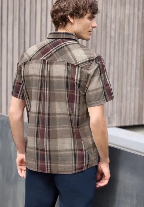 Een man van achteren in een geruit kortmouwen shirt voor een houten wand.