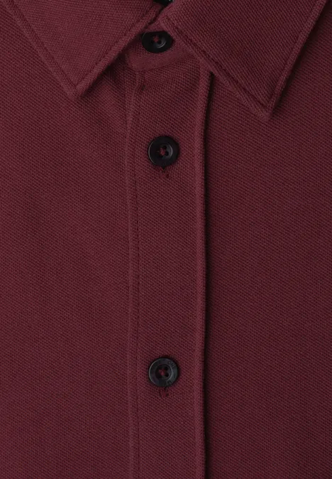 Close-up van een bordeauxrood overhemd met knopen en kraag.