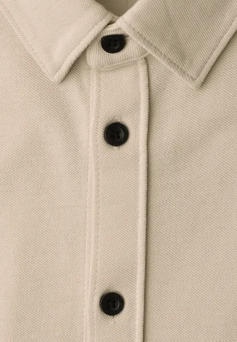 Beige Jacke mit Kragen und drei schwarzen Knöpfen in Nahaufnahme.