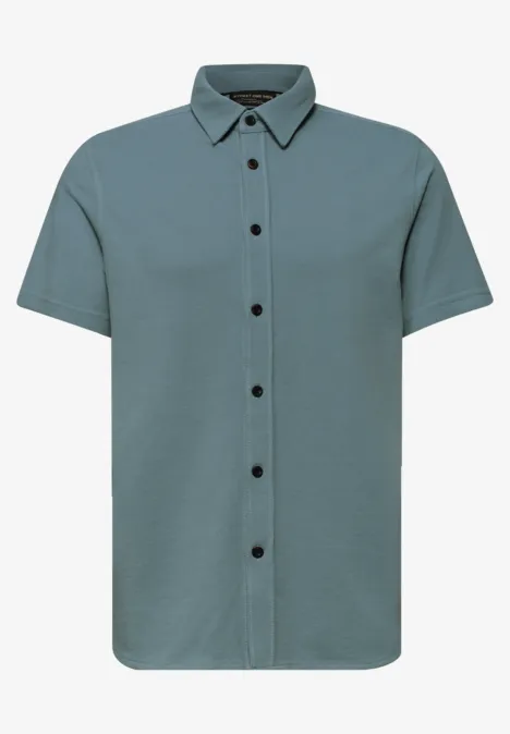 Kurzarm-Hemd in mattem Grünblau mit durchgehender Knopfleiste und schwarzen Knöpfen.