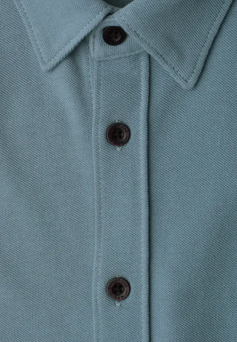 Nahaufnahme eines türkisfarbenen Poloshirts mit Kragen und drei schwarzen Knöpfen.