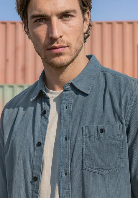Effen corduroy overhemd met lange mouwen vintage blue Een jonge man in spijkerhemd en wit T-shirt voor gekleurde containers.