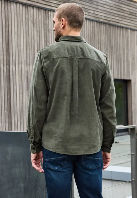 Effen corduroy overhemd met lange mouwen light moss green Man van achteren in groen corduroy overhemd en jeans voor een houten gevel.