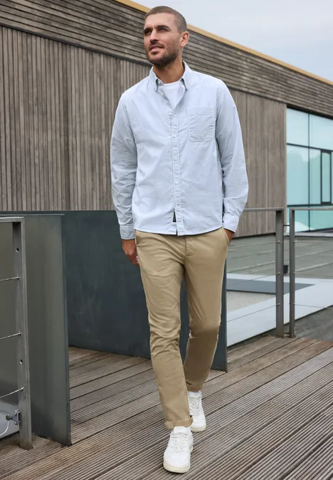 Overhemd met lange mouwen en streepjespatroon bright white Een man in een lichtblauw hemd, beige broek en witte sneakers loopt over een houten wandelpad.