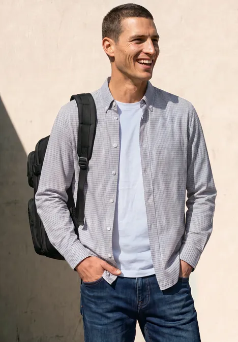Langarm Popeline Hemd mit Print bright white Ein lächelnder Mann in Jeans, weißem T-Shirt und hellgrauem Hemd trägt einen schwarzen Rucksack vor einer hellen Wand.