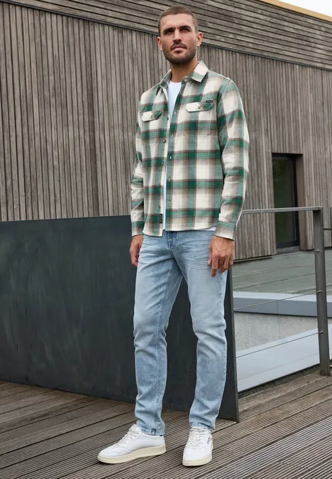 Overhemd met lange mouwen, borstzakken en ruitjespatroon bright white Een man staat op een houten terras voor een gevel, draagt een groen geruit overhemd, lichte jeans en witte sneakers.