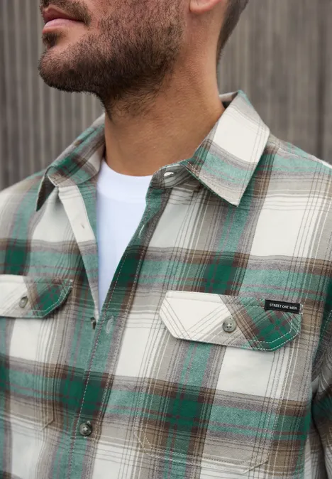 Overhemd met lange mouwen, borstzakken en ruitjespatroon bright white Close-up van een man in een geruite groene, bruine en witte blouse met open kraag en wit T-shirt eronder.