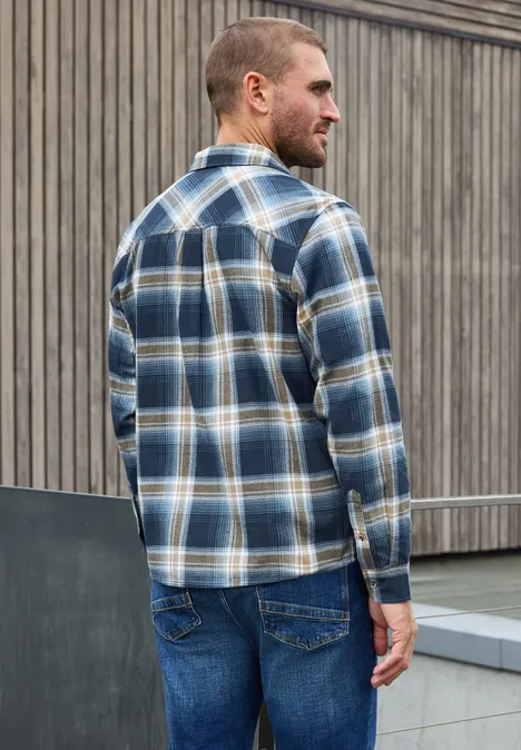 Langarm Hemd mit Brusttaschen und Karomuster dark ink blue Ein Mann steht seitlich und wendet sich ab, trägt ein blau-weiß kariertes Hemd und Jeans vor einer hölzernen Wand.
