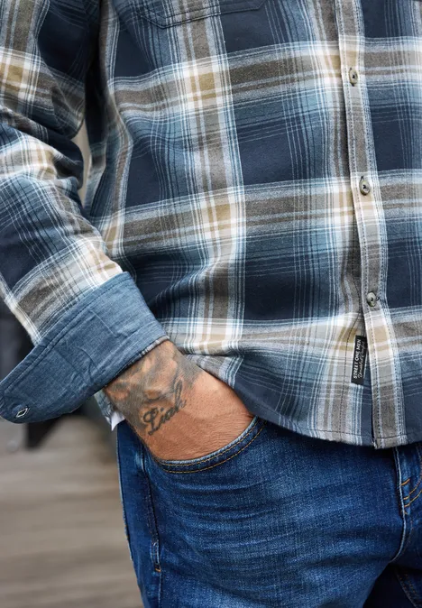 Langarm Hemd mit Brusttaschen und Karomuster dark ink blue Ein Mann trägt ein blau kariertes Hemd, steckt die Hand in die Jeans und zeigt ein Tattoo am Handgelenk.