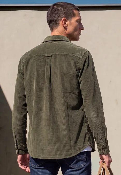 Rückansicht eines Mannes in khakigrüner Cord-Hemdjacke, lässig stehend, Blick zur Seite.
