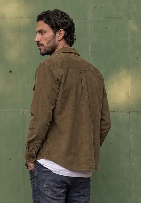 Ein Mann mit brauner Jacke und Jeans blickt über die Schulter vor einer grünen Wand.