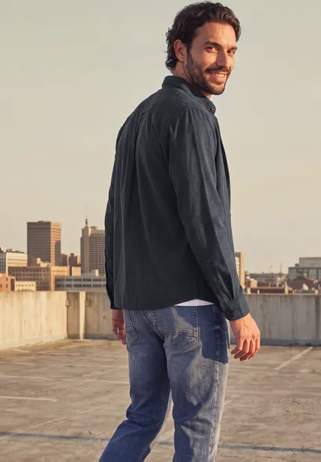 Langarm Twill Hemd mit Brusttasche basic black Ein Mann in Jeans und Jacke steht auf einem Dach und blickt über die Stadt.