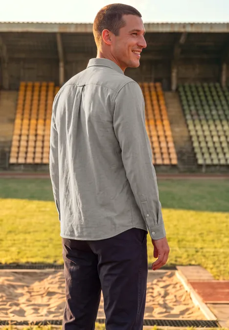 Chemise à manches longues en sergé avec poche poitrine antique beige Ein Mann im grauen Hemd steht lächelnd im Stadion, Rücken zur Kamera, Blick über die Schulter.