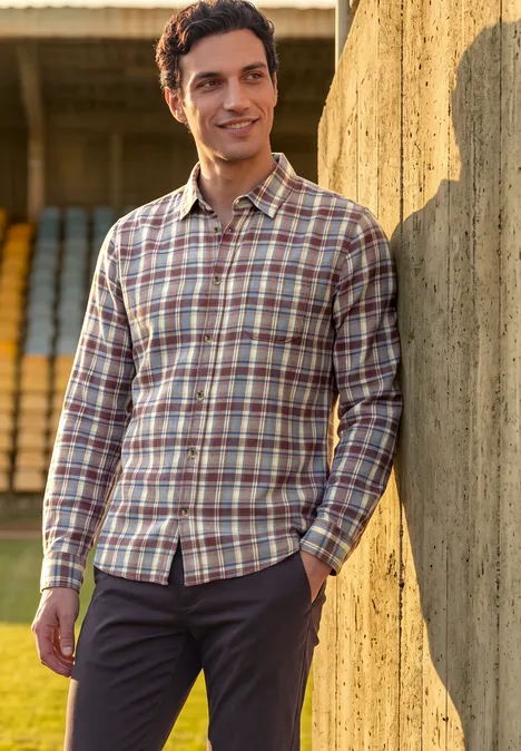 Chemise en flanelle à manches longues à carreaux raw copper red Ein Mann in karierter Hemd lehnt lässig an einer Betonwand vor Stadiontribüne.