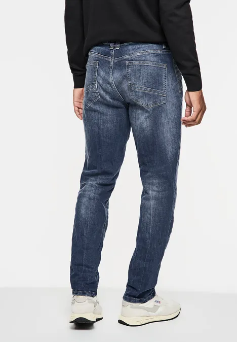 Homme en jean bleu et baskets blanches vu de dos, pull noir.