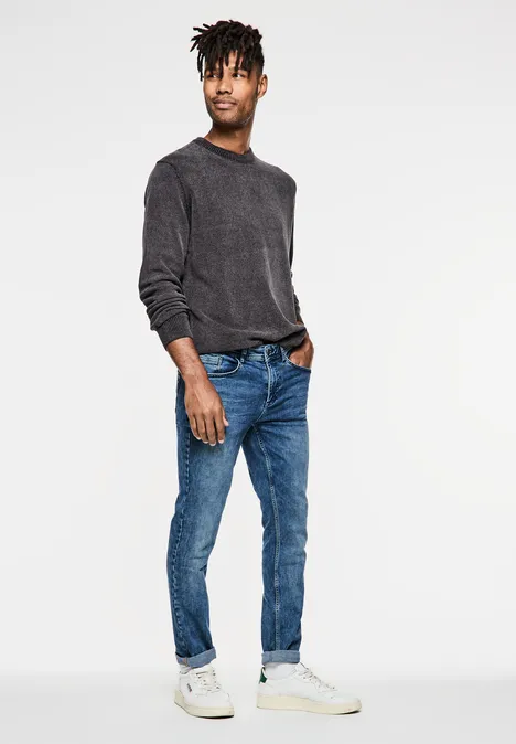 Homme en pull sombre, jean bleu et baskets blanches pose simplement.