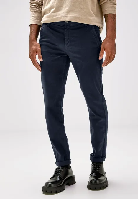 Homme en pantalon bleu foncé, haut beige et chaussures noires.