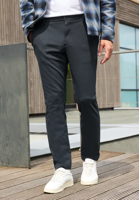 Chino aus elastischem Jersey mit Flexbund dark ink blue Ein Mann trägt dunkelgraue, schmale Hose und weiße Sneaker auf einer Holzterrasse vor einem modernen Gebäude.
